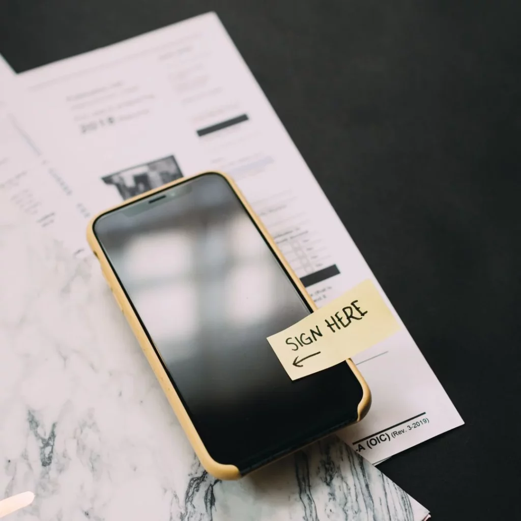 Smartphone lies on a table with the post it notice SIGN HERE