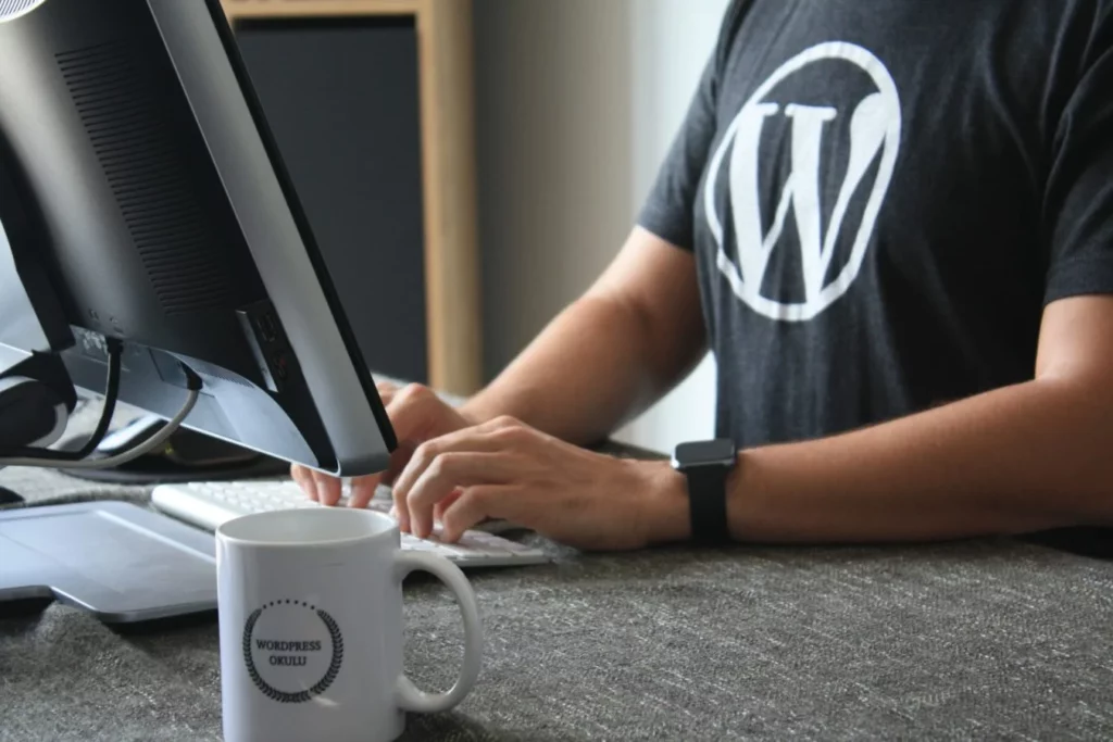 Man with a WordPress shirt sits in front of the screen and types on his keyboard.