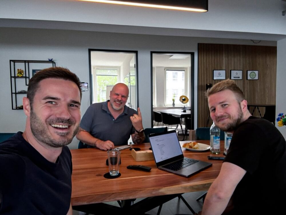 Mark Weisbrod, Remkus de Vries, and Jakob Trost smiling and talking during a strategy session at the Greyd office, with a laptop and whiteboard in the background.