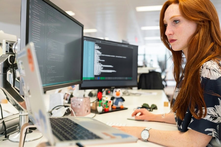 Female developer working at a desk with several screens