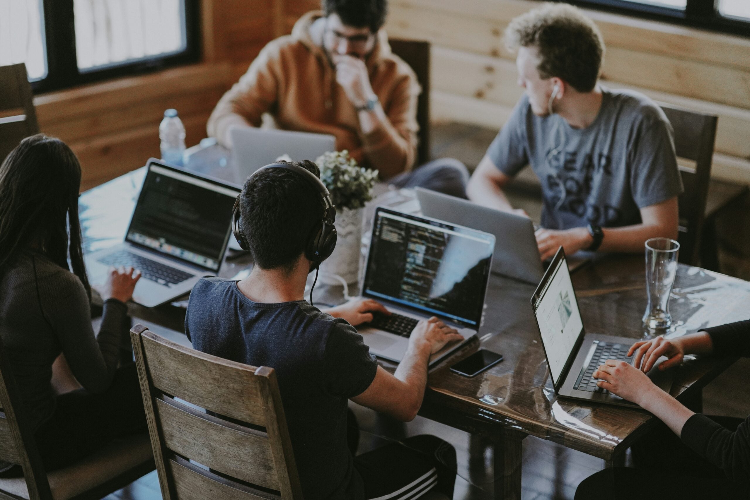 Five people working on laptops around a wooden table, with code visible on several of the screens.
